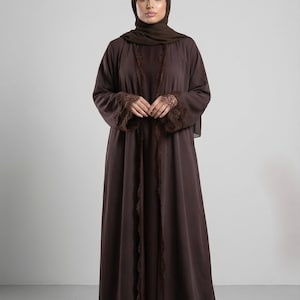 May include: A dark brown abaya and hijab. The abaya has lace detailing on the sleeves and front edges. This modest outfit is an elegant style, suitable for formal occasions.
