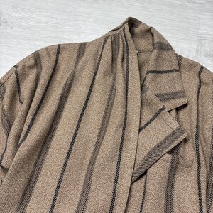 May include: A tan blazer with vertical black stripes. The blazer has a notched lapel and a single-breasted design. The fabric has a textured appearance.