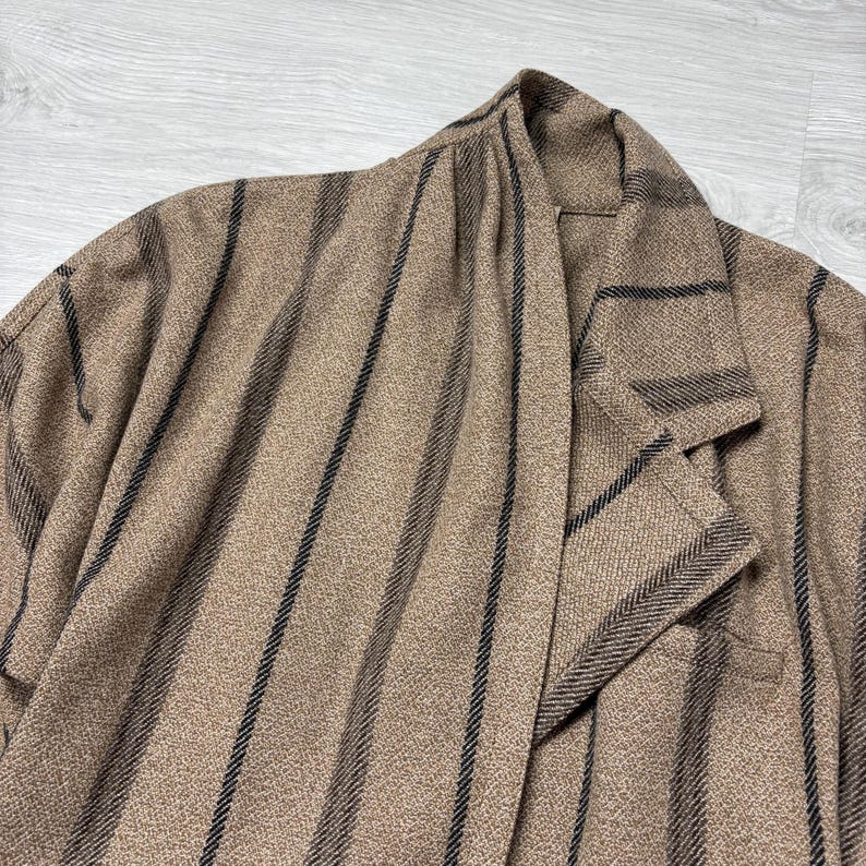 May include: A tan blazer with vertical black stripes. The blazer has a notched lapel and a single-breasted design. The fabric has a textured appearance.