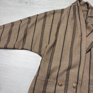 May include: A brown blazer with vertical black stripes. The blazer has a relaxed fit with a wide sleeve and two gold-colored buttons. The fabric has a textured appearance.