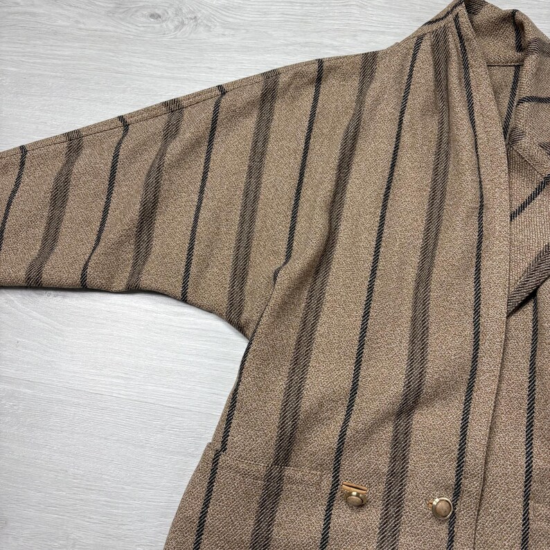May include: A brown blazer with vertical black stripes. The blazer has a relaxed fit with a wide sleeve and two gold-colored buttons. The fabric has a textured appearance.