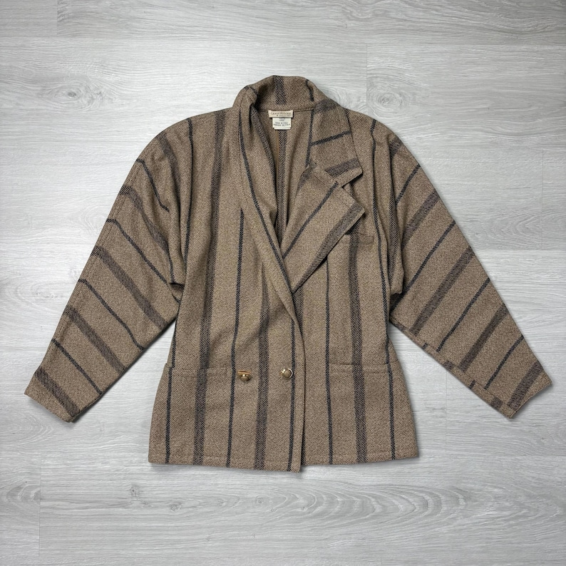 May include: A brown blazer with vertical black stripes. The blazer has a double-breasted design with two gold-colored buttons and two front pockets. The jacket has a notched lapel and long sleeves.
