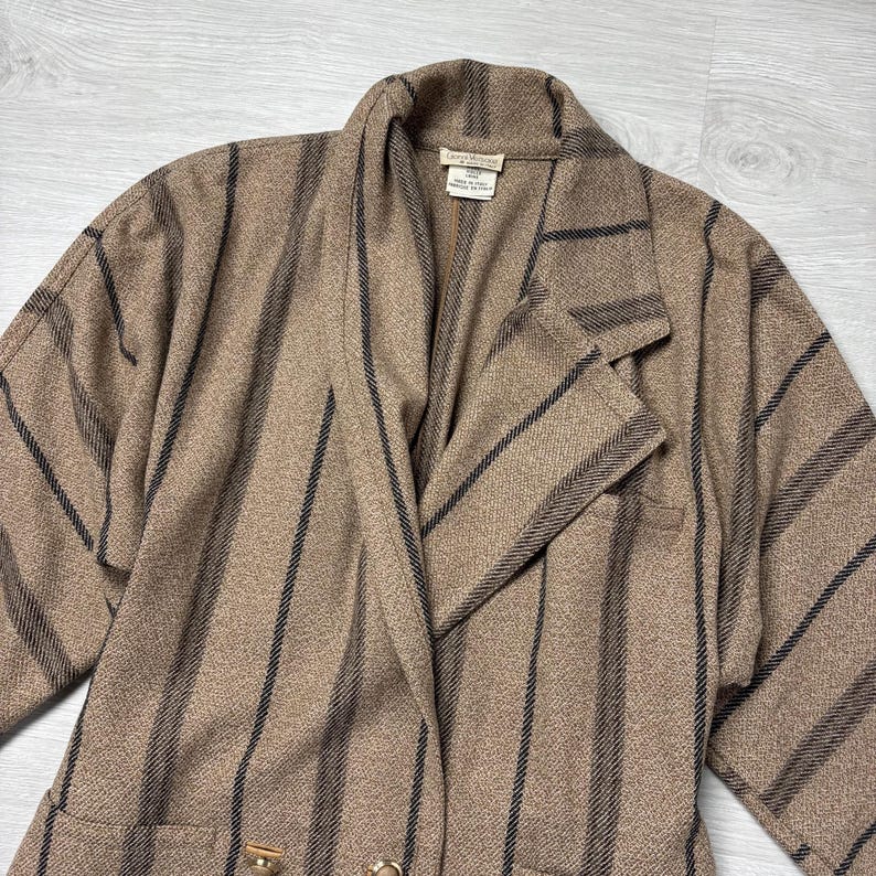 May include: A tan blazer with vertical black stripes. The blazer has a notched collar, two front pockets, and gold-colored buttons. The fabric appears to be a woven material.