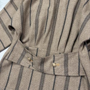 May include: A tan and black striped jacket with a tailored waist and gold-colored buttons. The jacket features a vertical stripe pattern and a structured design, suggesting a vintage or classic style. The fabric appears to be a woven material.