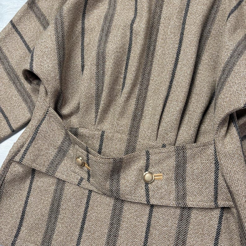 May include: A tan and black striped jacket with a tailored waist and gold-colored buttons. The jacket features a vertical stripe pattern and a structured design, suggesting a vintage or classic style. The fabric appears to be a woven material.