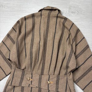 May include: A tan and black striped coat with a belted waist and gold-colored buttons. The coat has a classic design with vertical black stripes against a tan background. The coat's collar is visible.