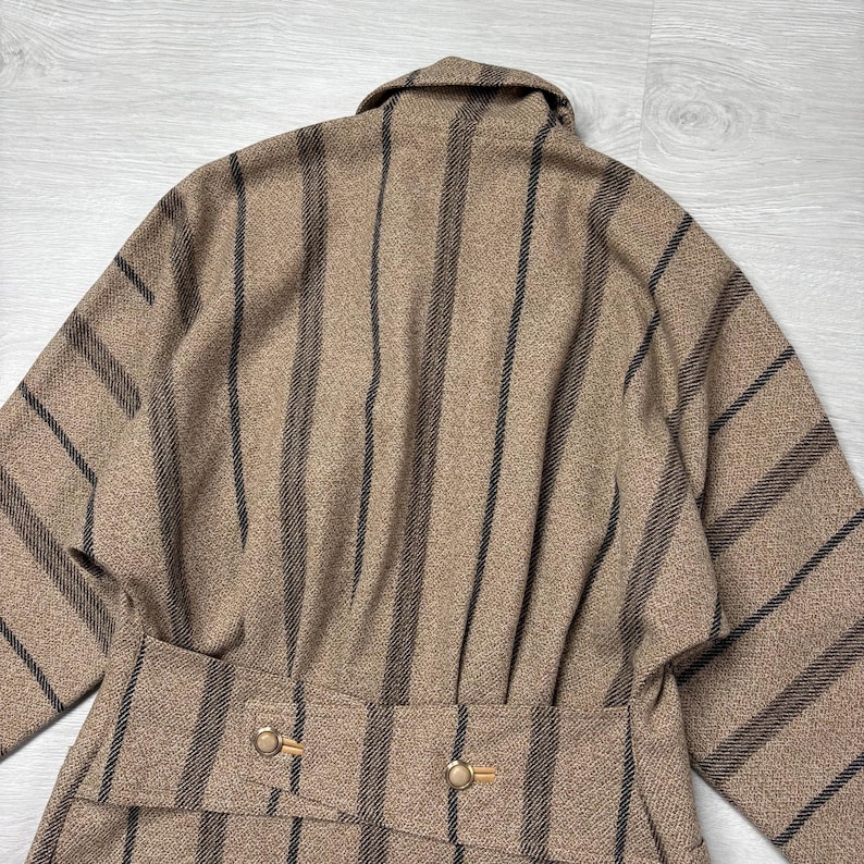 May include: A tan and black striped coat with a belted waist and gold-colored buttons. The coat has a classic design with vertical black stripes against a tan background. The coat's collar is visible.