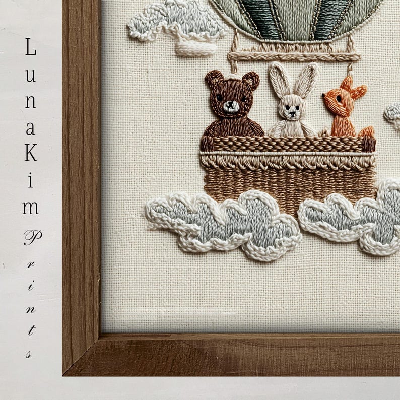 May include: Embroidered artwork featuring a hot air balloon with a bear, bunny, and fox in a woven basket. The balloon is green and tan, with white clouds below. The artwork is framed in a brown wooden frame. The text "Luna Kim Prints" is on the left side.