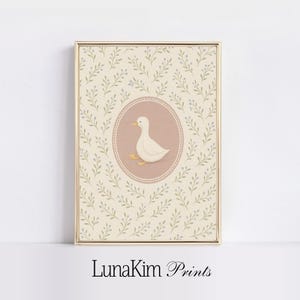 Puede incluir: Un pato blanco con un pico rosa y patas amarillas se representa en un c&iacute;rculo rosa sobre un fondo crema con un patr&oacute;n floral verde claro y morado. El texto "LunaKim Prints" est&aacute; en la parte inferior de la imagen.