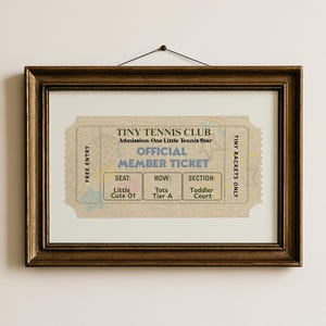 May include: A framed print featuring a vintage-style ticket design. The ticket, labeled "TINY TENNIS CLUB," has sections for seat, row, and section, with the text "OFFICIAL MEMBER TICKET." The frame is a dark, ornate wood.