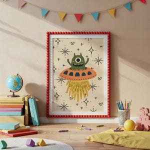以下が含まれることがあります： オレンジ色のUFOに乗った緑色の宇宙人のイラストが描かれた額入りのアートプリント。星とハートが描かれたクリーム色の背景。赤いフレームにはビーズの縁取りがあり、子供部屋の装飾に遊び心を加えています。