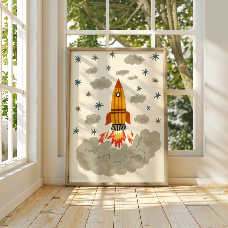 May include: A framed vertical wall art print featuring a yellow and orange rocket ship launching into space. The rocket is surrounded by grey clouds and blue and brown star shapes, with a large plume of grey smoke and red flames at the base.