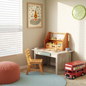 May include: A wooden desk with a light blue drawer, a matching wooden chair, and a wooden desktop organizer containing small toys. A red double-decker bus toy sits on the floor next to a round blue rug and a pink pouf, with a rocket ship wall art.