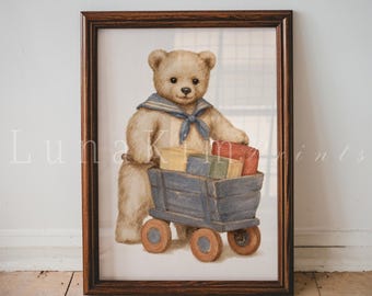 Könnte beinhalten: Ein gerahmter Kunstdruck, der einen hellbraunen Teddybären mit blauem Matrosenkragen zeigt. Der Bär steht und zieht einen blauen Holzwagen, der mit drei rechteckigen Blöcken in Gelb, Blau und Rot beladen ist, eingefasst in einem dunklen Holzrahmen.