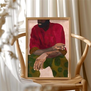 Puede incluir: Una impresi&oacute;n art&iacute;stica enmarcada que presenta una figura sentada con una camisa roja y pantalones verdes estampados. La obra de arte tiene una paleta de colores c&aacute;lidos y se exhibe en una silla de madera, creando un ambiente acogedor.