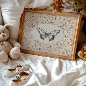 May include: A framed print with a delicate butterfly design on a light beige background with a floral pattern. The butterfly is black and white and is centered in an oval shape. The frame is made of light wood.