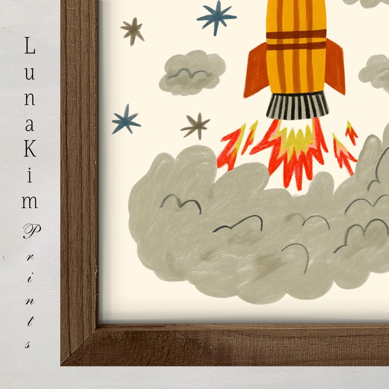 May include: A framed art print featuring a yellow rocket ship with orange fins launching into space, surrounded by gray clouds, red and yellow flames, and blue and brown stars. The text "Luna Kim Prints" is visible on the left side of the frame.