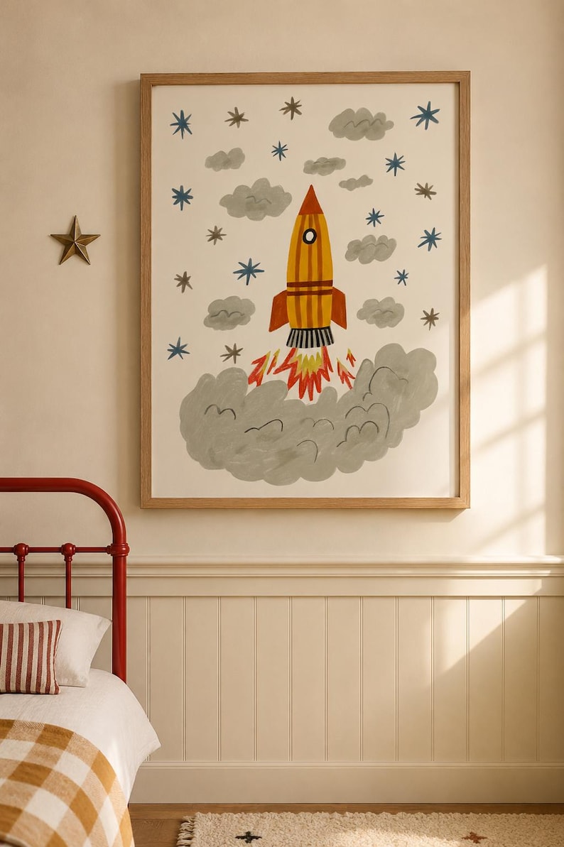 May include: A framed wall art print featuring a yellow and orange rocket ship launching into space. The illustration includes grey clouds, blue and brown stars, and a large grey smoke plume at the base. The artwork is enclosed in a light wood frame.