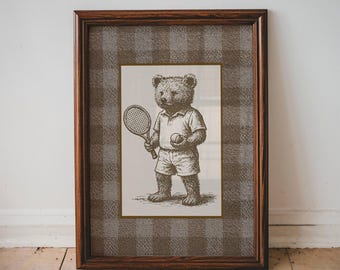 Könnte beinhalten: Gerahmter Druck mit einer Vintage-Illustration eines Teddybären beim Tennisspielen. Der Bär trägt Tennisbekleidung und hält einen Schläger und einen Ball. Der Rahmen ist dunkelbraun und der Hintergrund hat ein Karomuster.