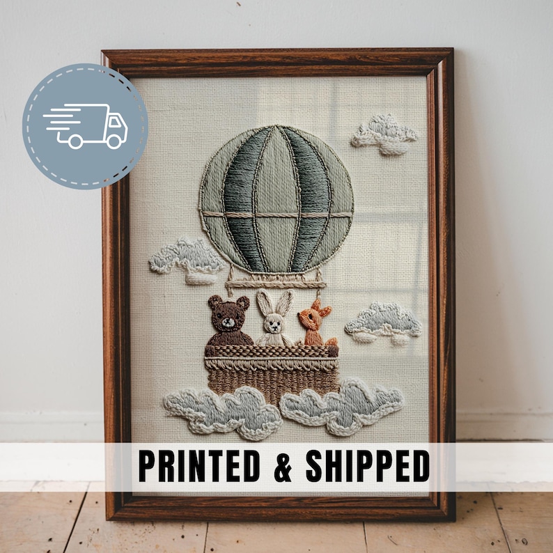 May include: Embroidered artwork in a wooden frame. The image features a hot air balloon with a bear, rabbit, and deer in the basket. The balloon is gray-green, and the clouds are light gray. The text "PRINTED & SHIPPED" is at the bottom.