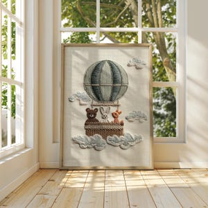 May include: Embroidered artwork of a hot air balloon with a blue and gray striped design, carrying a basket with a bear, rabbit, and deer. The artwork includes fluffy cloud details and is framed in a light wood.