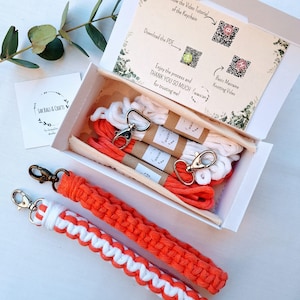 May include: A macrame keychain kit with orange and white cord, metal clasps, and instructions. The kit includes a box with spools of cord, and two finished keychains. The text on the box says "SAK BAGS & CRAFTS".