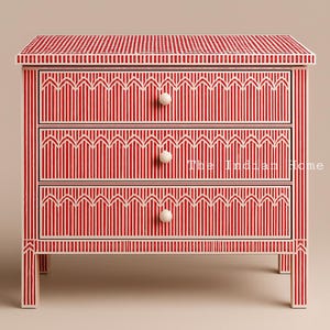 Op de afbeelding: Een rode en witte gestreepte kist met drie laden van beeninleg. De laden hebben een geometrisch patroon en witte knoppen.