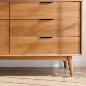 A handcrafted mid-century modern teak wood dresser with spacious drawers, featuring elegant curved drawer fronts and tapered legs. The dresser is made from solid natural teak with rich warm grains, placed in a bright minimalist room with white walls, soft natural light, a framed abstract artwork, two ceramic vases, and a textured white rug on light wood flooring. Modern, Scandinavian, and Japandi-inspired wooden furniture for premium home interiors.