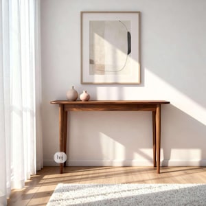 Könnte beinhalten: Eine Holzkonsolentisch mit warmbraunem Finish, mit einem langen, schmalen Design und vier konischen Beinen. Zwei kleine Vasen in neutralen Farbtönen stehen auf der Tischplatte unter einem gerahmten abstrakten Kunstdruck. Der Raum hat eine weiße Wand und einen weißen Teppich.