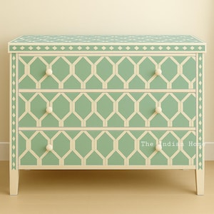 May include: A three-drawer chest of drawers with a geometric pattern in light green and cream. The chest has white knobs and is set on four legs. The text "The Indian Home" is visible on the bottom right.