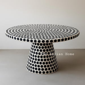 Op de afbeelding: Een ronde, witte tafel met een zwart stippenpatroon op de bovenkant en de basis. De tafel is gemaakt van bot en heeft een uniek, modern ontwerp.