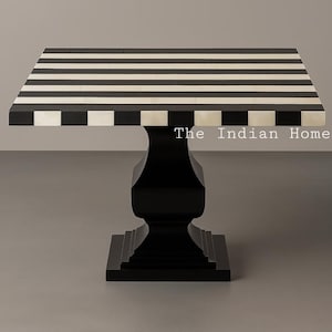 Könnte beinhalten: Ein quadratischer Tisch mit schwarz-weiß gestreifter Tischplatte und schwarzem Sockel. Die Tischplatte hat abwechselnd schwarze und weiße Streifen. Der Sockel ist einfarbig schwarz, mit einem dekorativen, geriffelten Design. Der Tisch ist ca. 76 cm hoch.