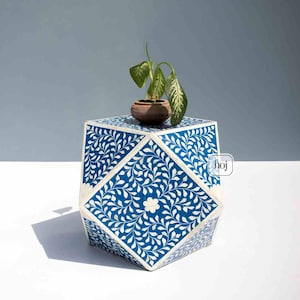 May include: A blue and white decorative side table with a geometric design. The table features a floral pattern and a small potted plant on top. The table is approximately 46 cm tall.