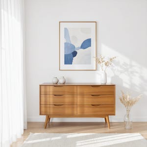A handcrafted mid-century modern teak wood dresser with spacious drawers, featuring elegant curved drawer fronts and tapered legs. The dresser is made from solid natural teak with rich warm grains, placed in a bright minimalist room with white walls, soft natural light, a framed abstract artwork, two ceramic vases, and a textured white rug on light wood flooring. Modern, Scandinavian, and Japandi-inspired wooden furniture for premium home interiors.
