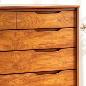 A handcrafted mid-century modern teak wood dresser with spacious drawers, featuring elegant curved drawer fronts and tapered legs. The dresser is made from solid natural teak with rich warm grains, placed in a bright minimalist room with white walls, soft natural light, a framed abstract artwork, two ceramic vases, and a textured white rug on light wood flooring. Modern, Scandinavian, and Japandi-inspired wooden furniture for premium home interiors.