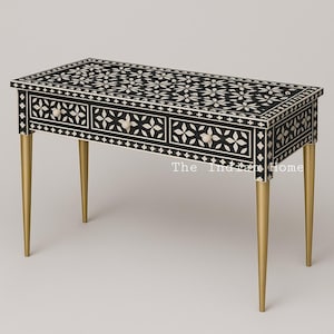 May include: A black and white bone inlay console table with three drawers and gold legs. The table top features a floral pattern. The text "The Indian Home" is visible on the table.