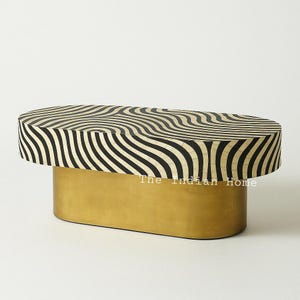 Puede incluir: Mesa de centro ovalada con tapa rayada en blanco y negro y base dorada. La mesa está hecha de incrustaciones de hueso y tiene un patrón ondulado único.