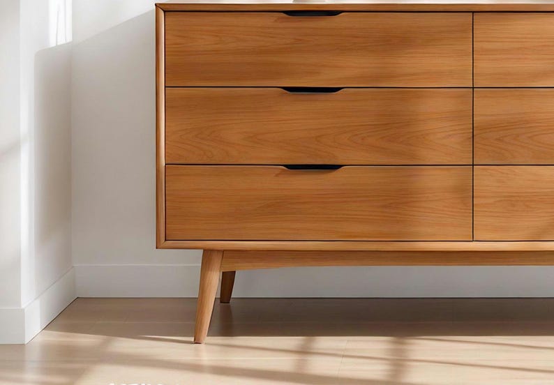 A handcrafted mid-century modern teak wood dresser with spacious drawers, featuring elegant curved drawer fronts and tapered legs. The dresser is made from solid natural teak with rich warm grains, placed in a bright minimalist room with white walls, soft natural light, a framed abstract artwork, two ceramic vases, and a textured white rug on light wood flooring. Modern, Scandinavian, and Japandi-inspired wooden furniture for premium home interiors.