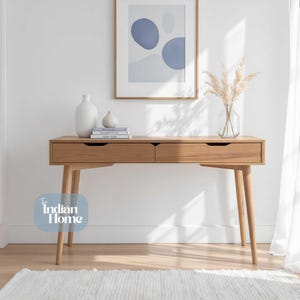 Könnte beinhalten: Ein helles Holzschreibtisch mit zwei Schubladen und konischen Beinen. Der Raum verfügt über einen gerahmten abstrakten Kunstdruck, dekorative Vasen und einen weißen Teppich. Der Schreibtisch ist etwa 120 cm lang.
