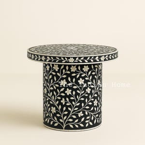 Puede incluir: Una mesa auxiliar redonda con una tapa redonda y una base cilíndrica. La mesa está hecha de incrustaciones de hueso y tiene un delicado diseño floral en blanco y negro.