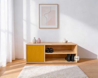 May include: A light wood shoe storage cabinet with a yellow door and open shelves. The cabinet has a rectangular shape and is placed on a wooden floor. The cabinet is decorated with small vases and a framed artwork.