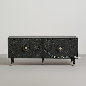 May include: Black wooden cabinet with carved floral design on the doors. The cabinet has gold-colored hardware and feet. The doors feature large, stylized flower patterns. The cabinet is a piece of furniture.