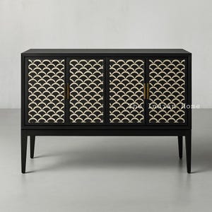Könnte beinhalten: Ein schwarzer Schrank mit drei Türen und goldenen Griffen. Jede Tür zeigt ein weiß-schwarzes geometrisches Muster. Der Schrank steht auf vier Beinen.