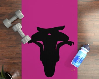 May include: A rectangular magenta yoga mat featuring a centered black silhouette of a person in a headstand yoga pose. Two light gray dumbbells are positioned on the left side of the mat, and a blue and white water bottle sits on the right side.
