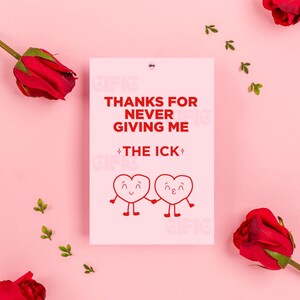 Puede incluir: Una tarjeta de felicitación blanca con el texto "THANKS FOR NEVER GIVING ME THE ICK" en rojo. Dos corazones de dibujos animados tomados de la mano en la parte inferior. La tarjeta está sobre un fondo rosa con rosas rojas y hojas verdes.