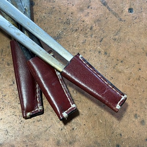 May include: Three brown leather sheaths with white stitching, each holding a silver metal tool.