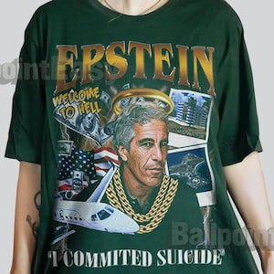 Puede incluir: Camiseta verde oscuro con un gráfico de un hombre con una cadena de oro y la palabra "EPSTEIN" en oro. La camiseta también incluye el texto "WELCOME TO HELL" y "I COMMITTED SUICIDE".