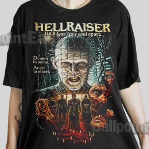 May include: Black t-shirt featuring the movie title "HELLRAISER" in gold lettering. The graphic includes a portrait of a character with a grid-like pattern on the head, surrounded by other figures and text. The text reads "He'll tear your soul apart."