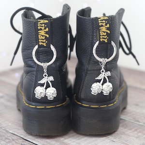 May include: A pair of black leather boots with silver skull cherry charms attached to the laces. The boots have a yellow "AirWair" label on the back.