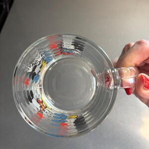 May include: A clear glass mug with a Mickey Mouse design. The mug features red stars and images of Mickey Mouse, Donald Duck, and Goofy.